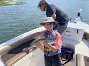 father and son on the front of bay boat in myrtle beach, south carolina with son holding a speckled sea trout  for a family friendly charter fishing