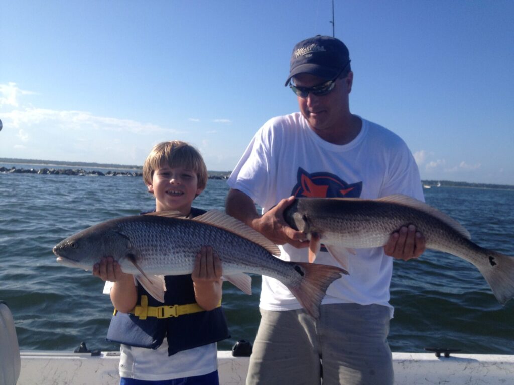 Kid and dad holding two red drum aka redfish on a myrtle beach inshore fishing charter