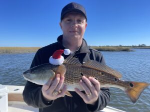 man holding a redfish with a Santa hat on. Merry Christmas from North Myrtle Beach Fishing Charters