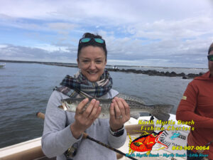 Gril holding a speckle3d sea trout on the bow of a boat out my the jetties with North Myrtle Beach Fishing Charters