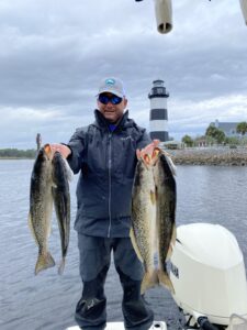 Myrtle Beach Fishing Guide Captain Keith Logan of North Myrtle Beach Fishing Charters on the boat holding 4 nice speckled sea trout  with light house in the background