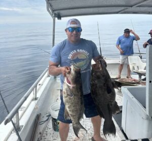 man on boat holding a gag grouper and scamp grouper while fishing on a myrtle beach deep sea fishing charters