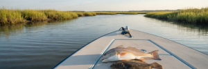 A shallow flats boat in a North Myrtle Beach marsh with a freshly caught red drum and flounder on deck at morning light