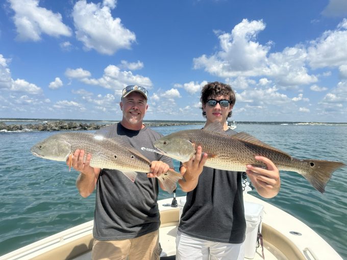 north-myrtle-beach-bull-redfish-jetty-fishing Two anglers holding large bull redfish aboard a fishing boat beside Little River rock jetty.